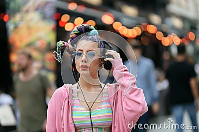 Fashion cool funky girl in headphones listening to music wearing colourful pink sweater and fancy sunglasses Stock Photo