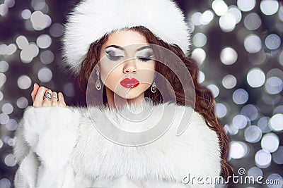 Fashion girl model posing in fur coat and white furry hat. Winter Beautiful Woman in Luxury clothes over boker Christmas Lights b Stock Photo