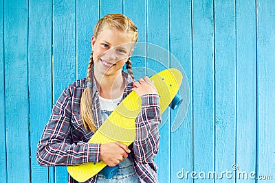 Stylish teenager wearing a summer jeans clothes, with skateboard having fun in city over colorful blue background Stock Photo