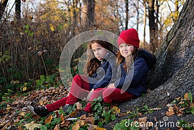 Fashion kids in autumn park. Close up lifestyle portrait of two beautiful caucasian girls outdoors, wearing cute trendy outfit in Stock Photo