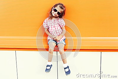 Fashion little girl child wearing a sunglasses and checkered shirt in city over colorful background Stock Photo