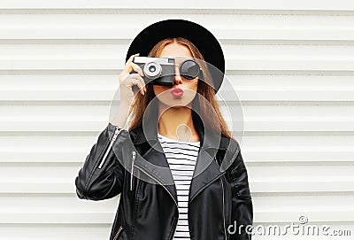 Fashion look, pretty cool young woman model with retro film camera wearing elegant black hat, leather rock jacket over white Stock Photo