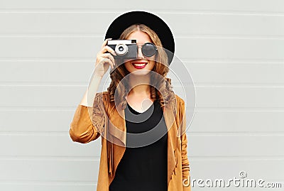 Fashion look, pretty cool young woman model with retro film camera wearing a elegant hat, brown jacket, curly hair outdoors Stock Photo