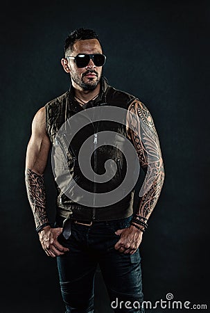 Fashion macho in trendy sunglasses. Tattoo model with beard on unshaven face. Bearded man with tattoo on strong arms Stock Photo