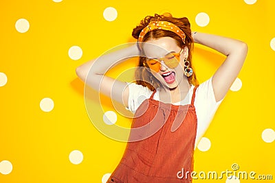 Fashion model girl over yellow polka dots background. Beauty stylish redhead woman posing in urban clothes and yellow sunglasses Stock Photo