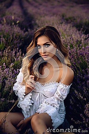 Beautiful girl with blond hair in elegant clothes posing in summer flowering lavender field Stock Photo