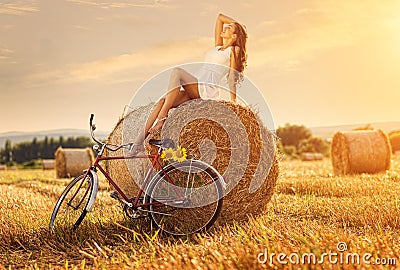 Fashion photo, beautiful woman sitting on a bale of wheat, next to the old bike Stock Photo