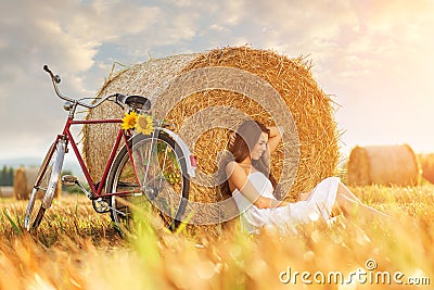Fashion photo, beautiful woman sitting in front of bales of wheat, next to the old bike Stock Photo