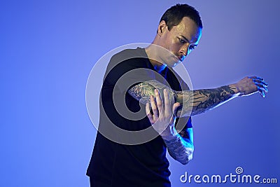 Fashion photoshoot of sport fit attractive man making arm stretch, tattooed hands, hipster look. Color flash studio light. Stock Photo