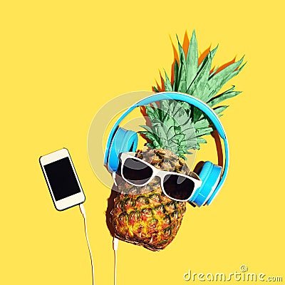 Fashion pineapple with sunglasses and headphones listens music on smartphone over yellow background Stock Photo