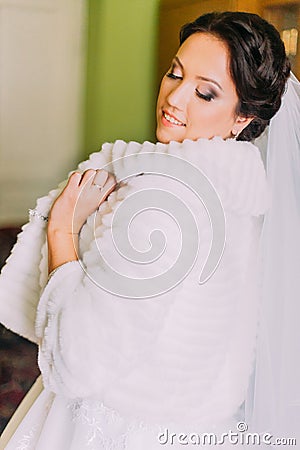 Fashion portrait of beautiful young happy bride in white fur coat indoor Stock Photo