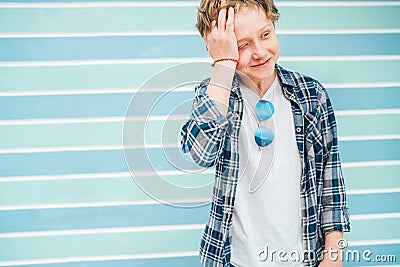 Fashion portrait of caucasian blue-eyed blonde hair 12 year old teenager boy dressed t-shirt and checkered shirt with sunglasses Stock Photo