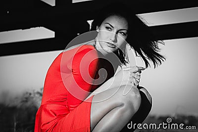 Fashion portrait of gorgeous sensual woman with dark hair wears elegant red dress. She is stting. Emphasis on red Stock Photo