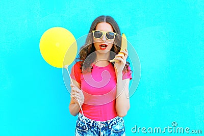 Fashion portrait pretty woman with banana and yellow a air balloon having fun over colorful blue background Stock Photo