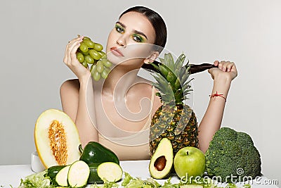 Fashion portrait of young attractive brunette woman that sits by the table with fruits and vegetables Stock Photo