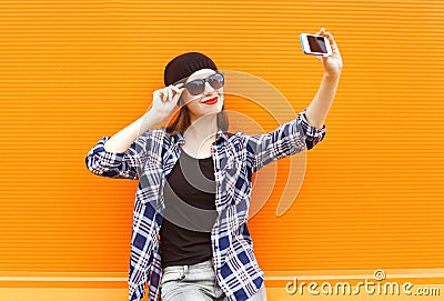 Fashion pretty cool girl makes selfie portrait on smartphone over colorful orange Stock Photo