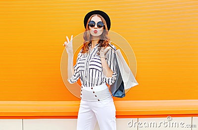 Fashion pretty cool young girl with shopping bags wearing a black hat white pants over colorful orange Stock Photo