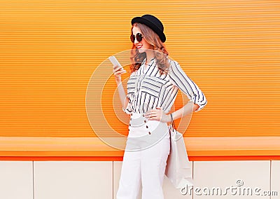 Fashion pretty happy young smiling woman model using smartphone with shopping bags wearing a black hat white pants over colorful Stock Photo