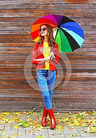 Fashion pretty woman with colorful umbrella wearing a red leather jacket and rubber boots in autumn over wooden background Stock Photo