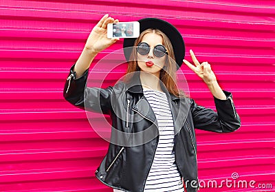 Fashion pretty woman makes self portrait on smartphone in black rock style over city pink Stock Photo