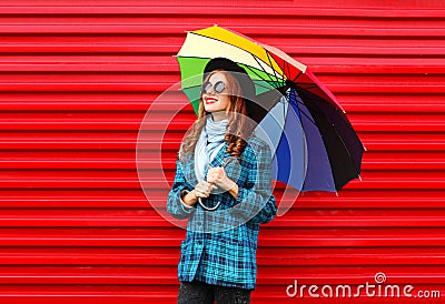 Fashion pretty young smiling woman holds colorful umbrella wearing black hat checkered coat jacket over red Stock Photo