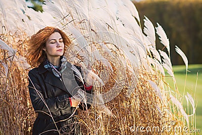 Fashion shooting, a girl in a coat against a background of reeds. Stock Photo