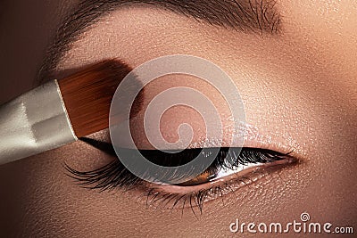 Fashion woman applying eyeshadow, mascara on eyelid, eyelash and eyebrow using makeup brush. Professional make-up artist Stock Photo