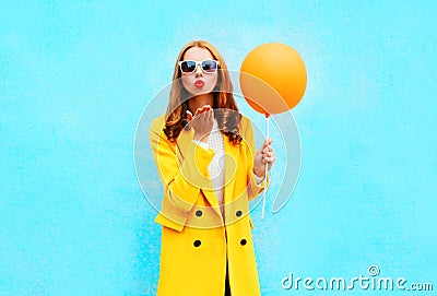 Fashion woman sends an air kiss holds balloon in a yellow coat Stock Photo