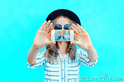 Fashion woman is taking photo self portrait on a smartphone in the city closeup screen over colorful blue Stock Photo