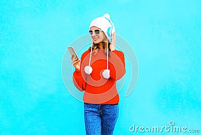 Fashion woman uses smartphone listens to music in wireless headphones in red sweater Stock Photo