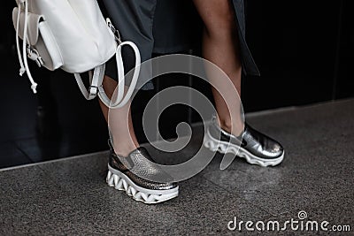 Fashion women clothes. Stylish women`s shoes. Casual design. Close-up of female legs in silver leather sneakers. Street style. Stock Photo