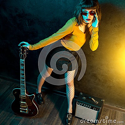 Fashion young hipster woman with curly hair with red guitar in neon lights. Rock musician is playing electrical guitar Stock Photo