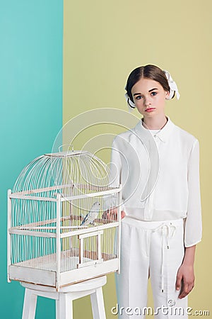 fashionable attractive girl in white outfit with parrot in cage on turquoise Stock Photo