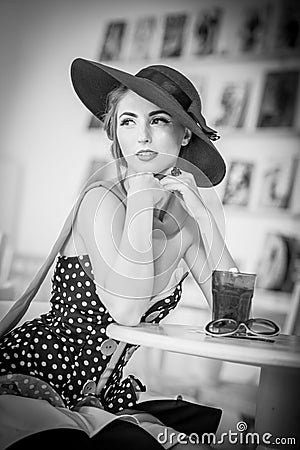 Fashionable attractive lady with hat and scarf sitting in restaurant, indoor shot. Young woman posing in elegant scenery Stock Photo