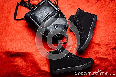 Black boots with a flat sole and black leather backpack on a red rag background Stock Photo