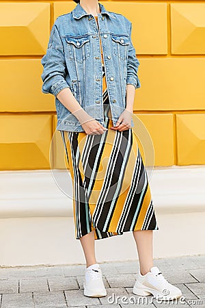 Fashionable female look with a denim blue jacket, a skirt with diagonal lines and white sneakers. Street fashion. Stock Photo