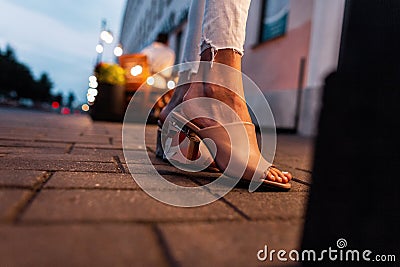 Fashionable girl in stylish beige summer shoes stands on a tile in the city in the evening, close up Stock Photo