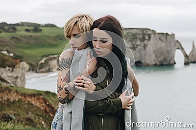 fashionable girlfriends embracing on beautiful cliff Etretat Stock Photo