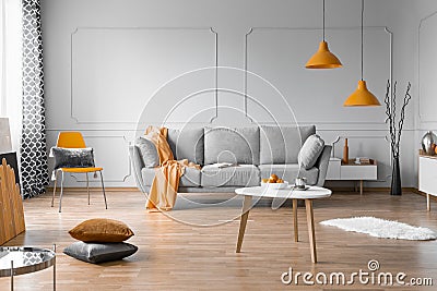 Fashionable living room interior design with grey couch, wooden coffee table and orange accents Stock Photo