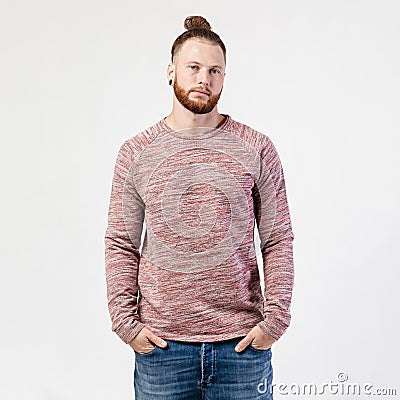 Fashionable man with beard and bun hairstyle dressed in pock-marked long sleeve sweater and jeans poses in the studio on Stock Photo