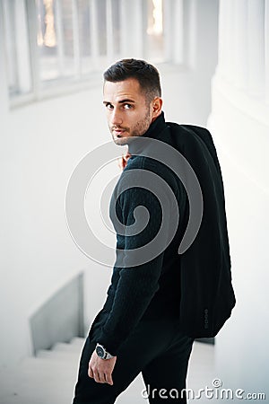 Fashionable man in a black stylish clothing outfit glancing back over bright sunlit architectural space Stock Photo