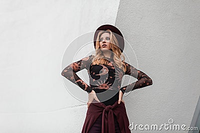 Fashionable red-haired young woman in a chic hat in a vintage patterned blouse with a purple cape at the waist is posing Stock Photo