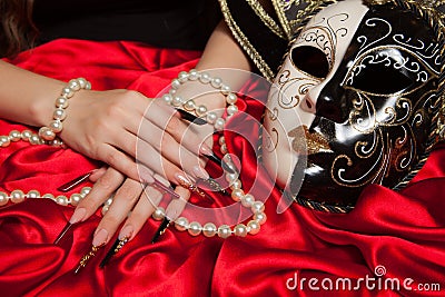 Fashionable stilettos nails design with Venetian buffoon mask, beads on red silk Stock Photo