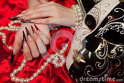 Fashionable stilettos nails design with Venetian buffoon mask, beads on red silk Stock Photo