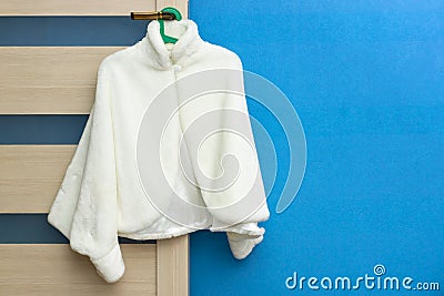Fashionable white female coat hanging on door handle on blue wall background Stock Photo