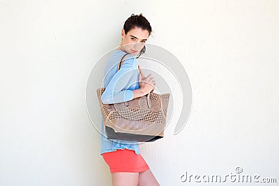 Fashionable young woman holding purse against white wall Stock Photo