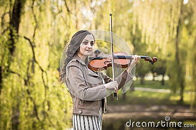 Fashionable young woman thoughtfully and dreamily plays the violin in the park Stock Photo