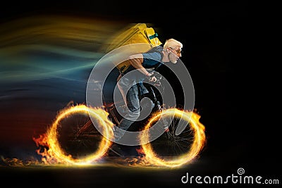 Fast delivery service - deliveryman on bicycle driving with order in fire on dark background Stock Photo