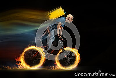 Fast delivery service - deliveryman on bicycle driving with order in fire on dark background Stock Photo