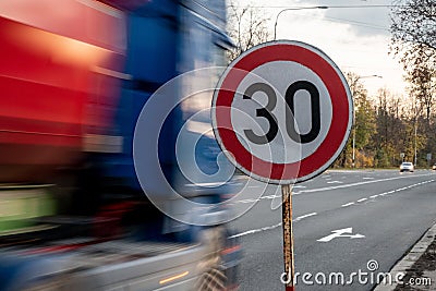 A fast driving blue speeding truck with motion blur effect near the traffic sign limiting the maximum speed to 30 kph Stock Photo